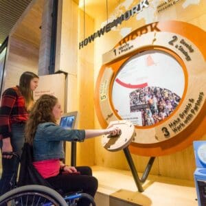 A lady in a wheelchair examines a display titled, "How We Work"