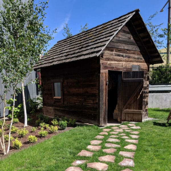 A raw-wood building with a coblestone path through the grass to it