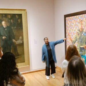 visitors look interested as a guide points something out about a painting